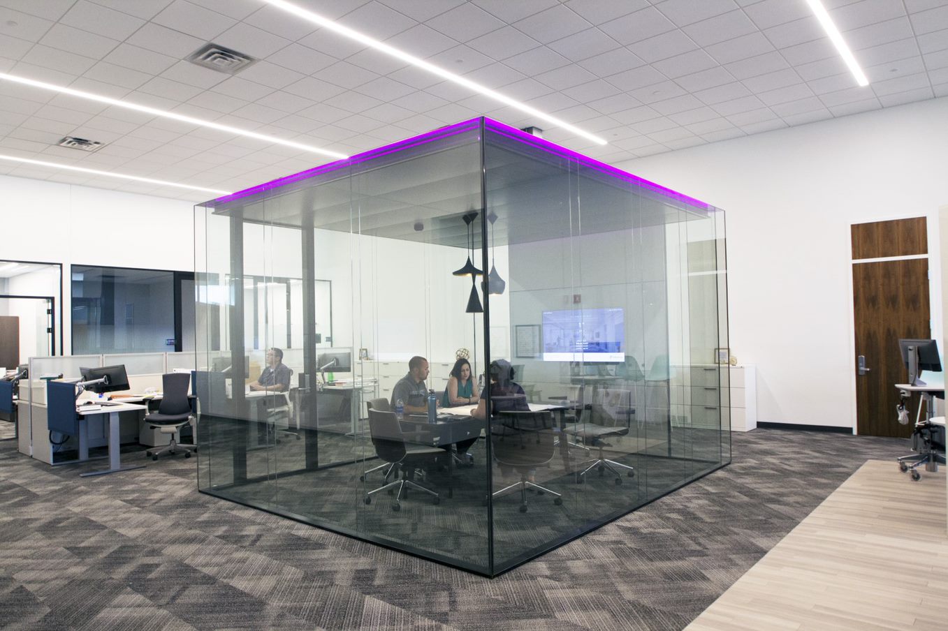 Glazen vergaderruimte binnen een kantoorruimte met 3 vergaderende mensen